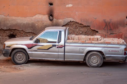 Old pickup car with heap of bricks in trunk parked on town street near shabby old building on sunny day