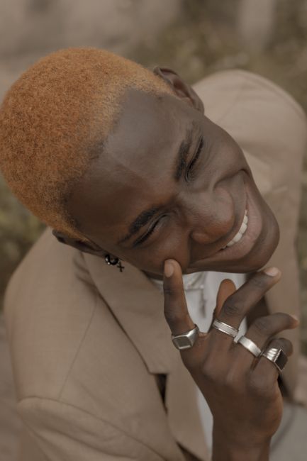 A joyful young adult with blonde hair smiling outdoors in a stylish portrait.