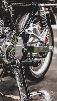 Detailed view of a motorcycle's kickstand and engine on a wet pavement, showcasing mechanical design.