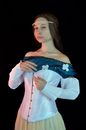 Serious feminine young lady with long brown hair in medieval dress with corset looking at camera against black background