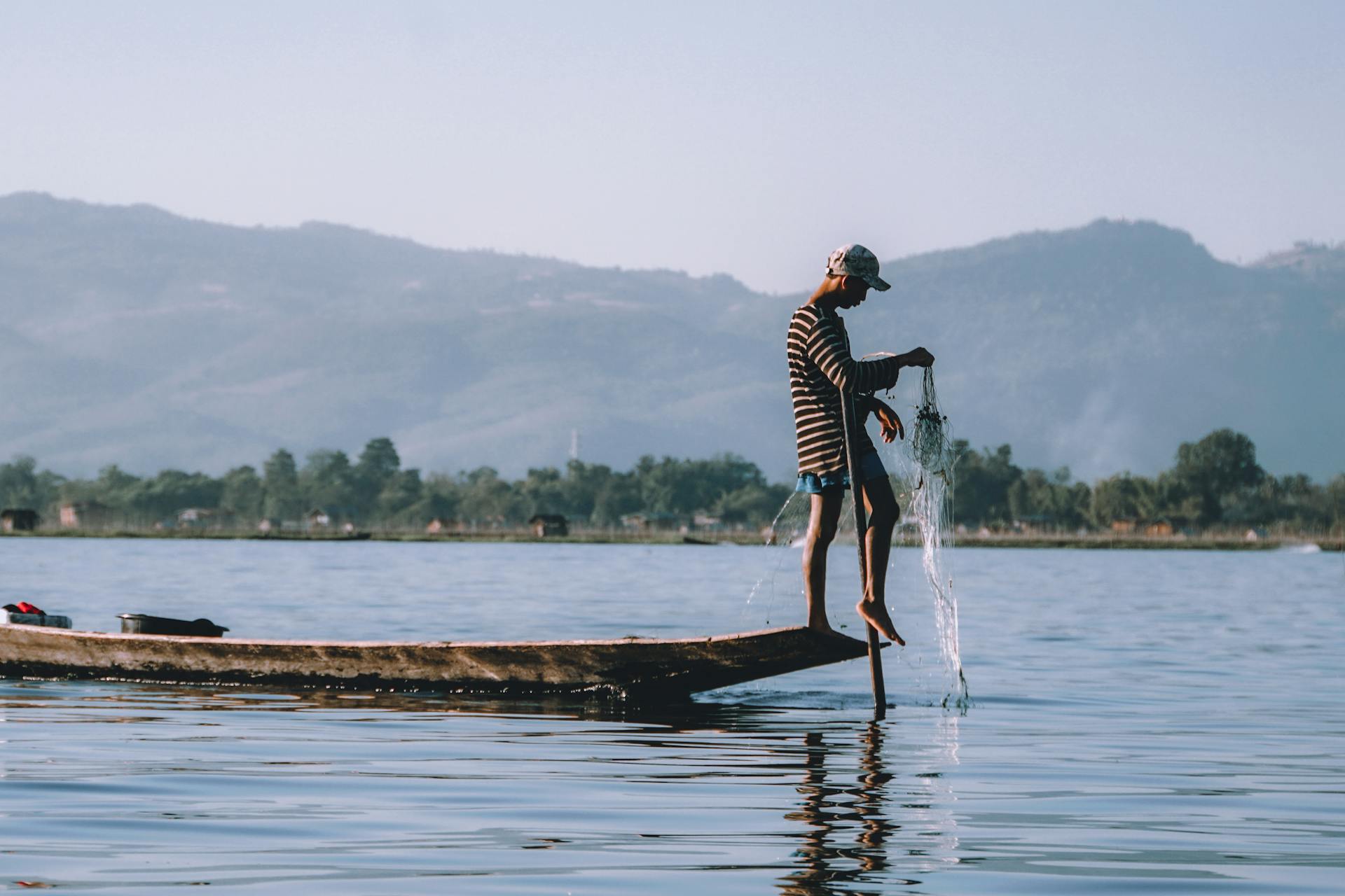 A traditional fisherman skillfully balancing on a wooden boat in a serene Myanmar lake.