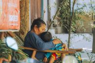 A Burmese grandmother lovingly embraces her grandchild in a peaceful outdoor setting.