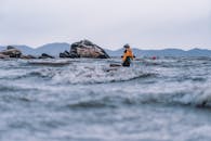 Person in Hat and Jacket Standing among Waves on Sea Shore