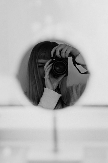 Artistic black-and-white self-portrait of a woman using a camera in front of a round mirror.