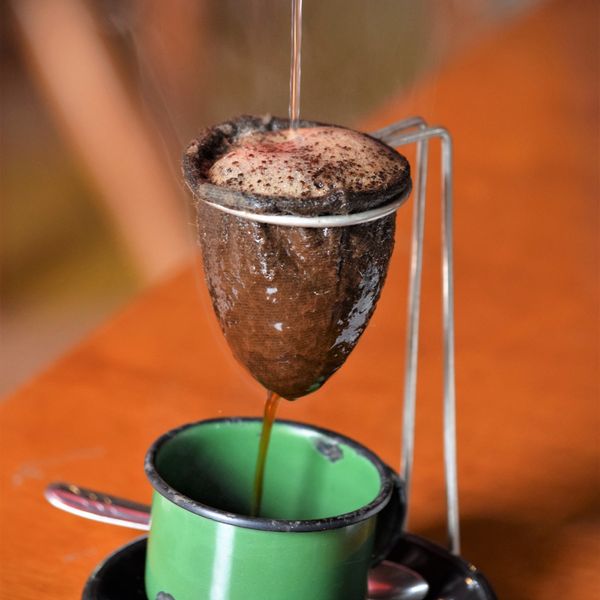 Café passando no coador de pano para uma caneca esmaltada verde