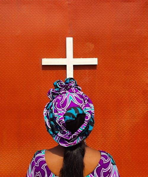 Woman in Colorful Turban Standing under Cross Nailed to Red Wall