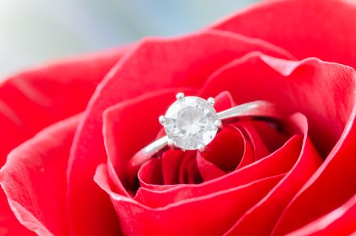 Free Close-up of a diamond engagement ring nestled in vibrant red rose petals, symbolizing love. Stock Photo