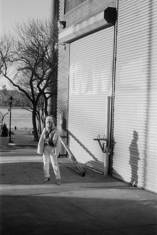 Grayscale Photo of a Woman Standing Beside Roll Up Door