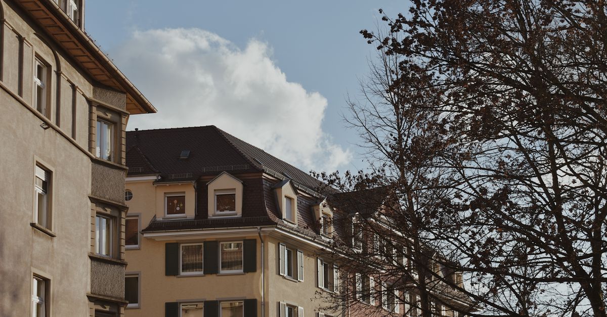 Low-angle shot of urban residential buildings and trees under a clear blue sky.