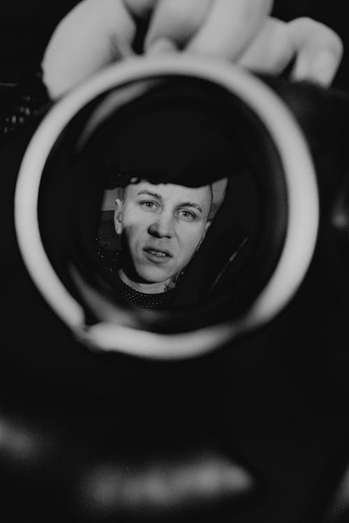 Black and white reflection of young man face looking at camera in round mirror and hand of crop person