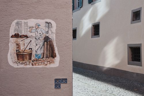Free A vibrant wall painting in a charming urban alleyway displays a baker scene on a rustic building. Stock Photo