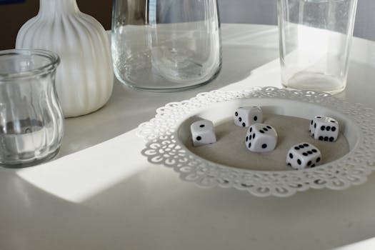 A creative still life featuring dice, glassware, and shadows on a white table.