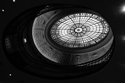 A detailed black and white photo of an ornate dome ceiling with stained glass and artistic patterns.