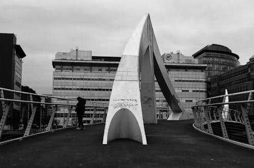 Grayscale Photo of a Person Standing on the Bridge