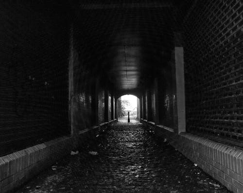 Фотография человека, идущего по туннелю в оттенках серого