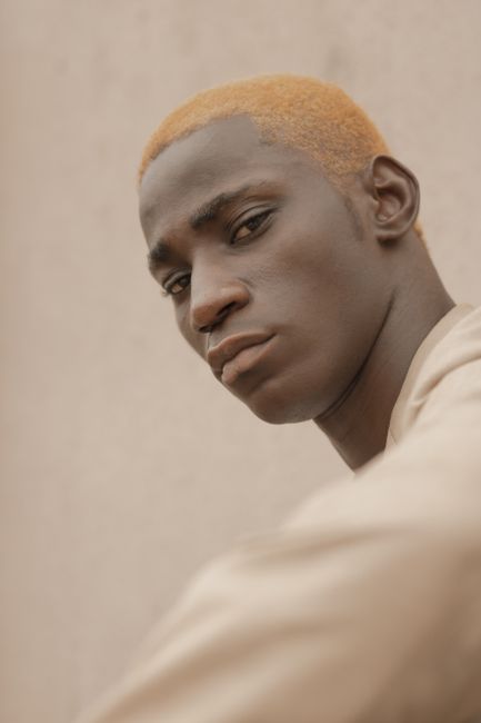 Expressive headshot of a black man with orange hair against a beige background.