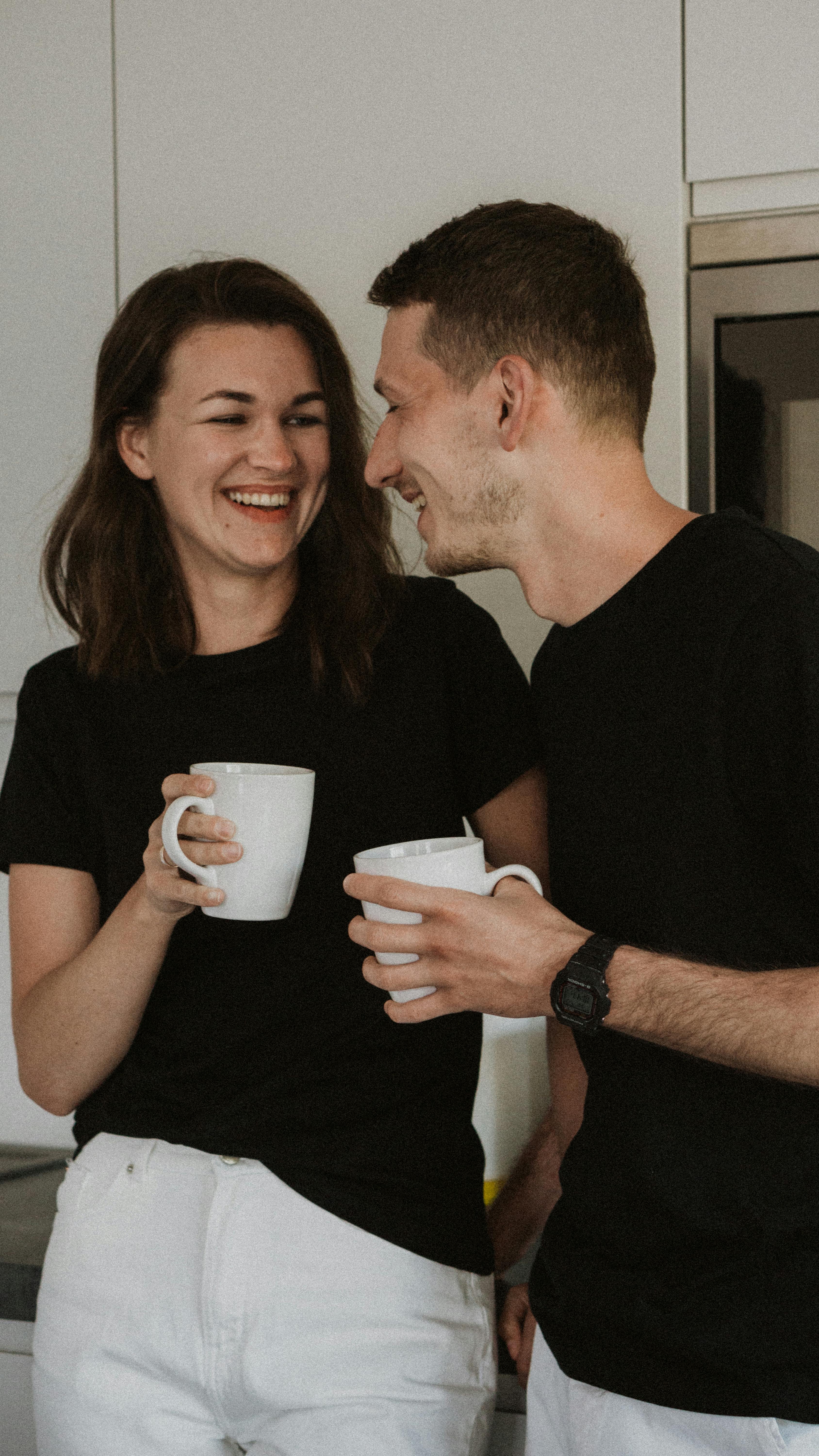 Happy couple enjoying coffee and laughter in a cozy kitchen setting.