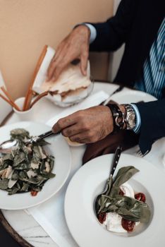 From above of crop unrecognizable male in stylish suit and wristwatch eating delicious salads with bread sticks while resting in restaurant terrace during lunch break