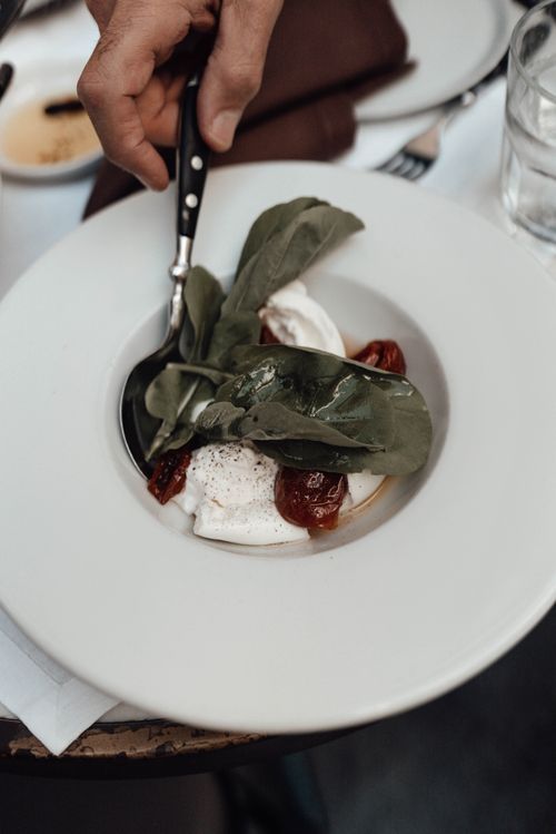 Free From above of crop anonymous male eating healthy salad with burrata cheese sun dried tomatoes and spinach in restaurant Stock Photo