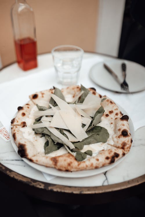 From above of delicious pizza with Parmesan cheese and spinach served on plate on round marble table on restaurant terrace