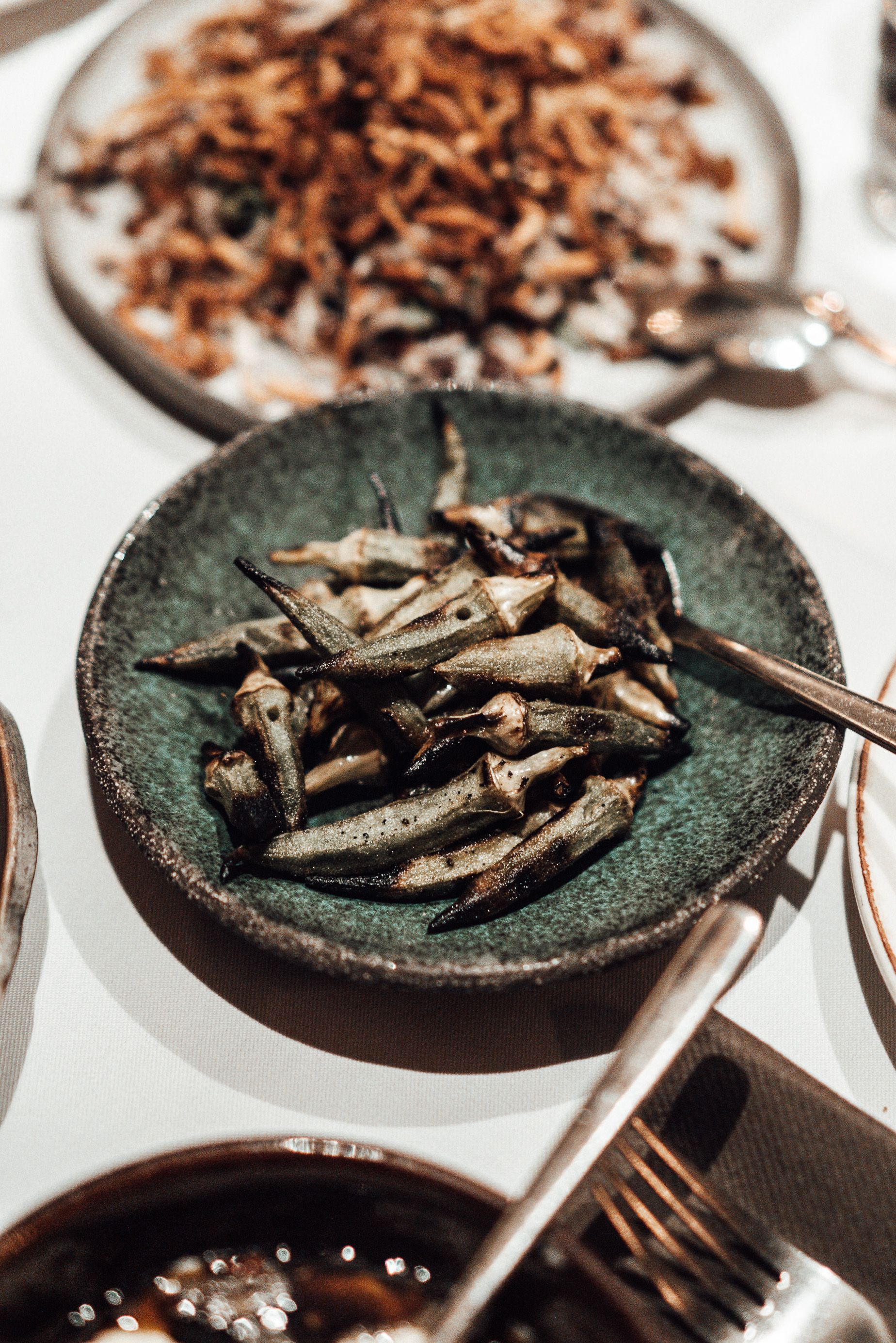 Charred roasted okra pods in a green ceramic bowl