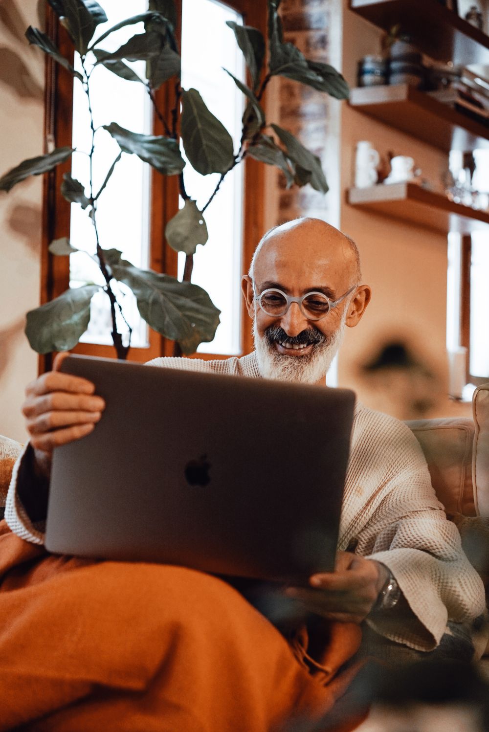 A smiling older man talking to a friend on a laptop video call