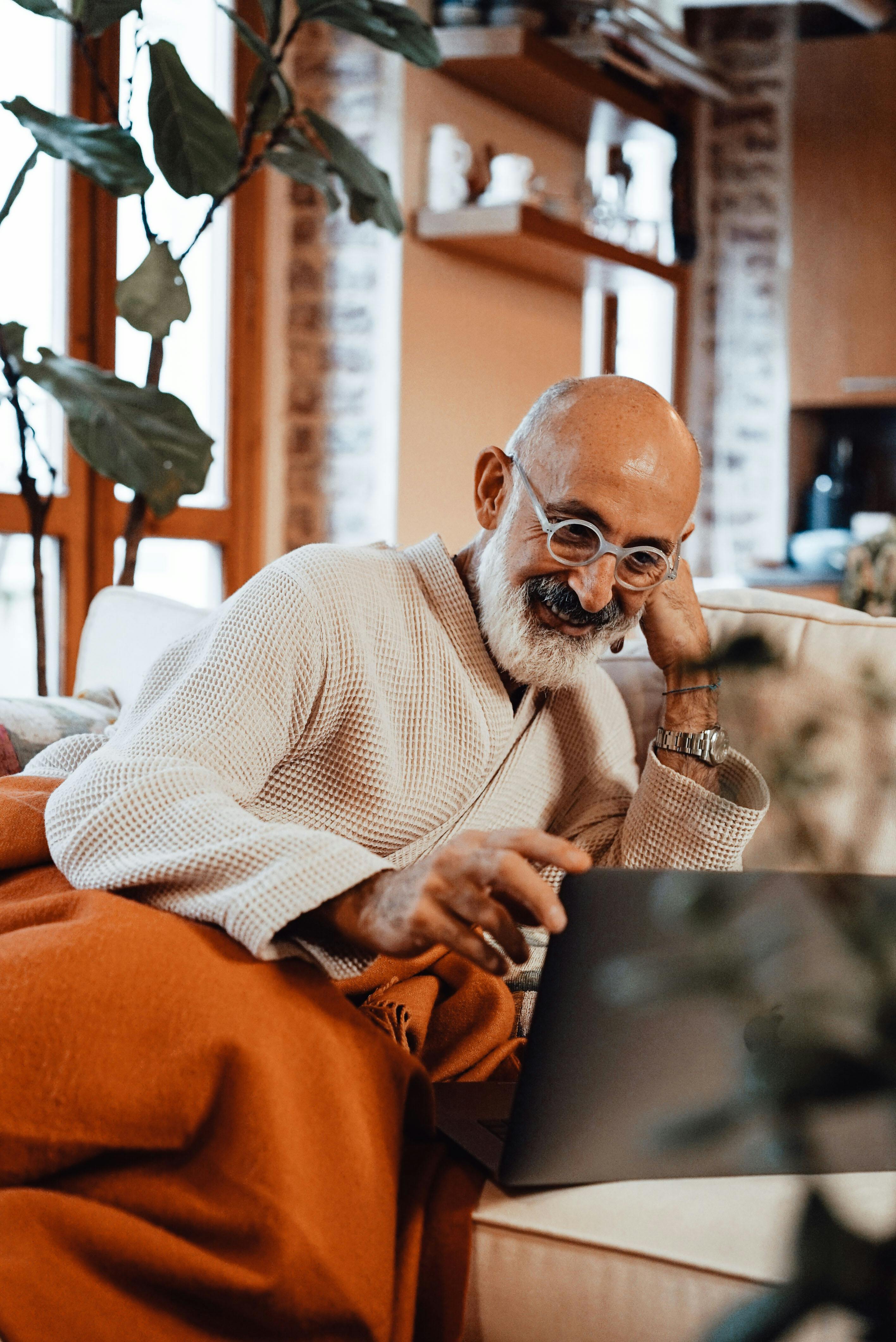 delighted senior ethnic man smiling while browsing netbook resting on sofa