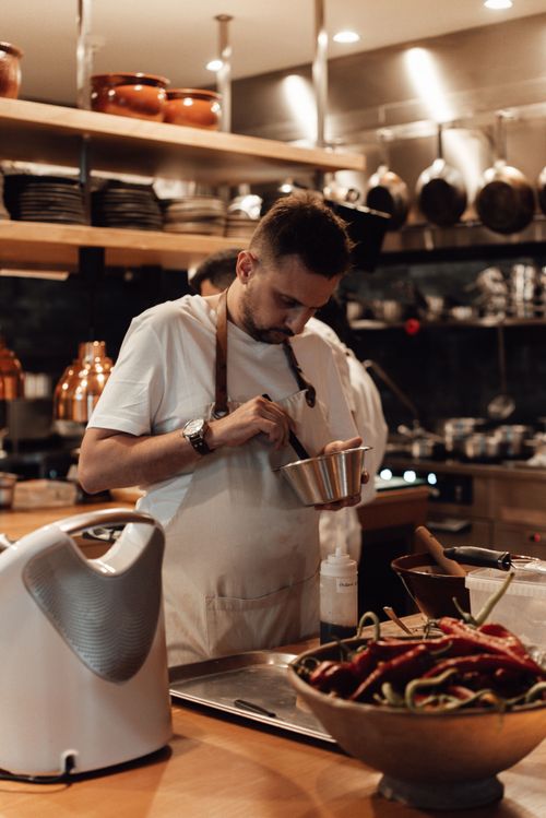 Free Concentrated young bearded male cook in t shirt and apron stirring ingredients in metal bowl while preparing food at table in restaurant kitchen Stock Photo