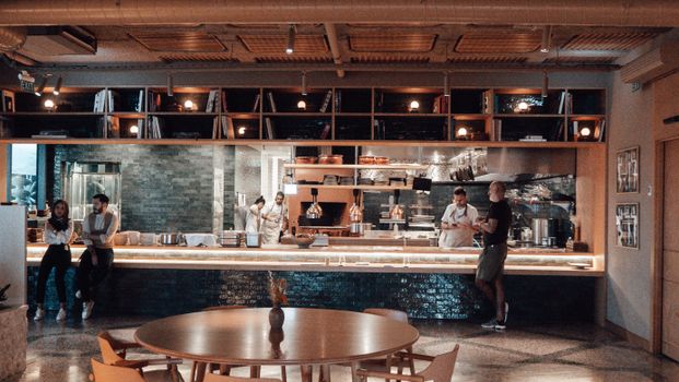 Unrecognizable cooks and bartenders standing at counter near anonymous male client making order in modern cafe