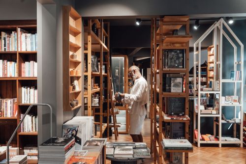 Free Side view of pensive senior ethnic man in stylish outfit standing among wooden bookshelves in modern bookstore Stock Photo