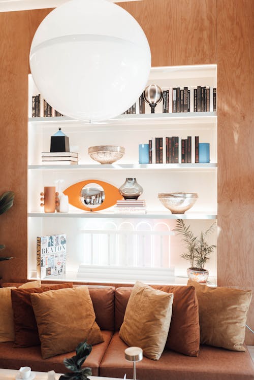 Free Comfortable sofa with cushions places near shelf with various decorative elements and books in modern living room Stock Photo