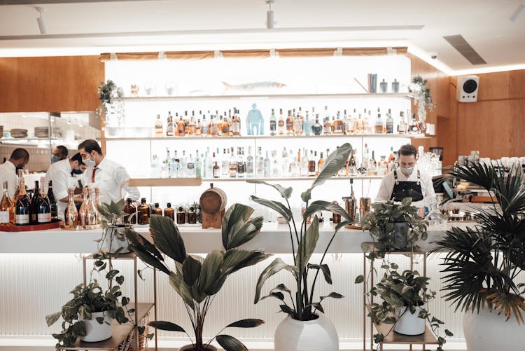 Unrecognizable Male Bartenders Standing At Counter Near Shelves With Various Drinks In Restaurant