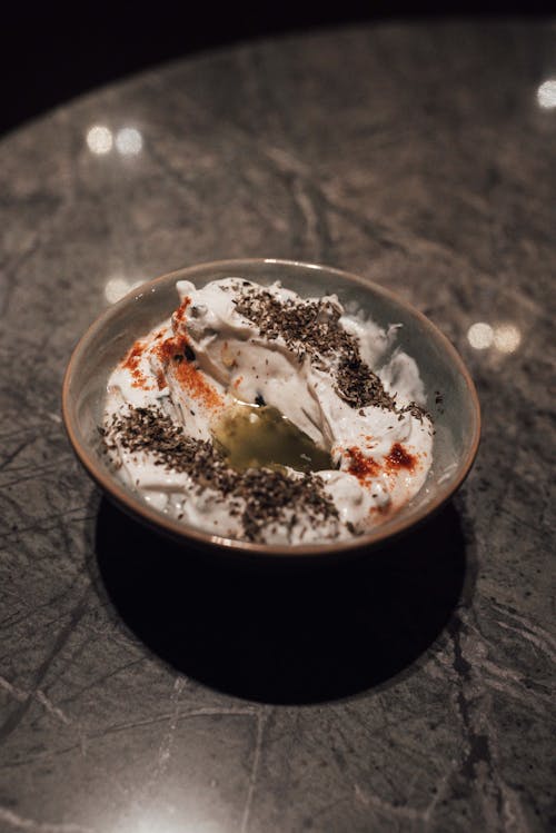 Free From above of bowl with appetizing spicy yogurt with red and black pepper served on gray table in restaurant Stock Photo