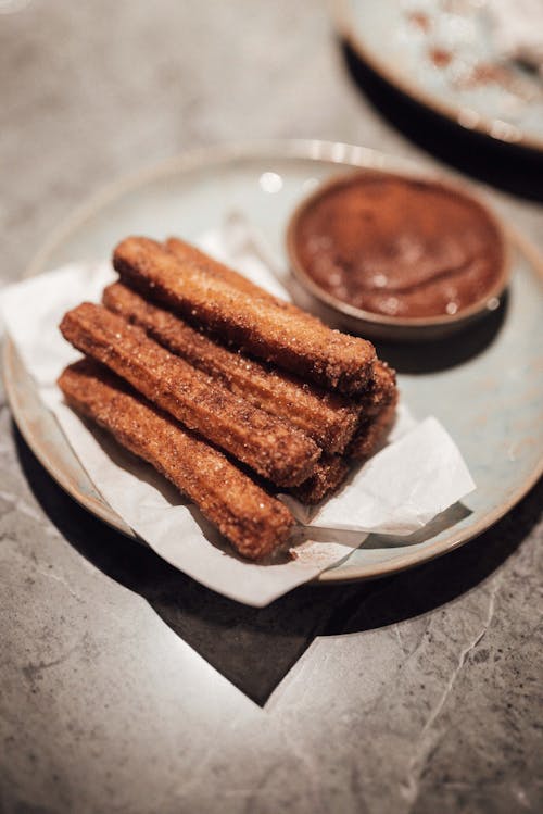 Delicious churros with chocolate sauce served on plate in cafe