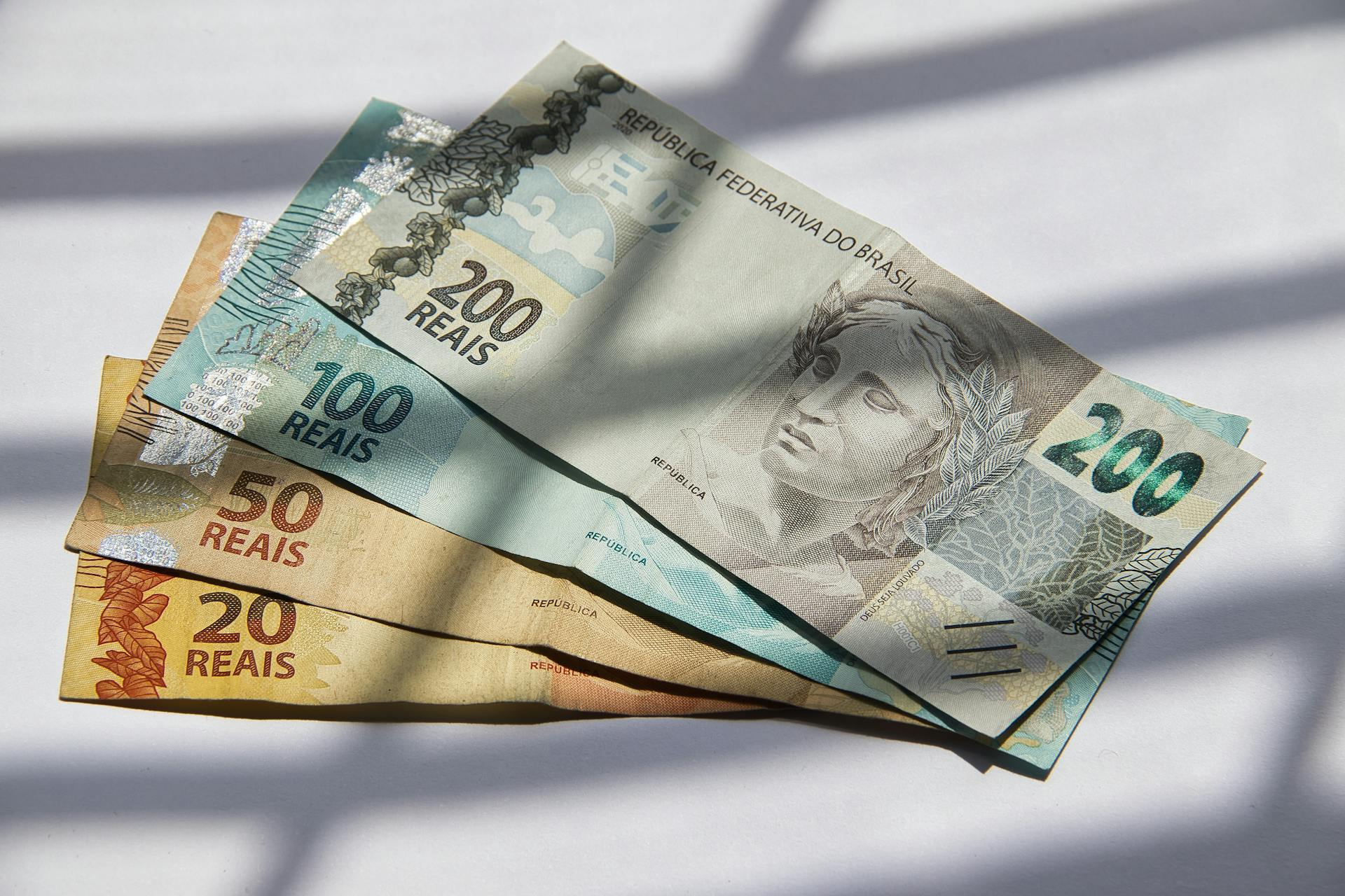 Various Brazilian real banknotes in sunlight, showcasing currency variety.