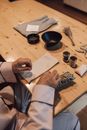 From above of crop anonymous male sitting at wooden table and making herbal smudge stick in room