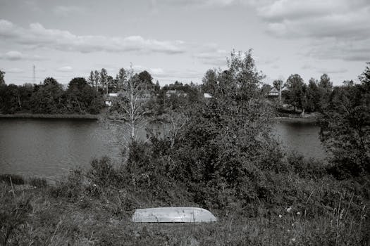 Black and white photo of a quiet lakeside with an abandoned boat.