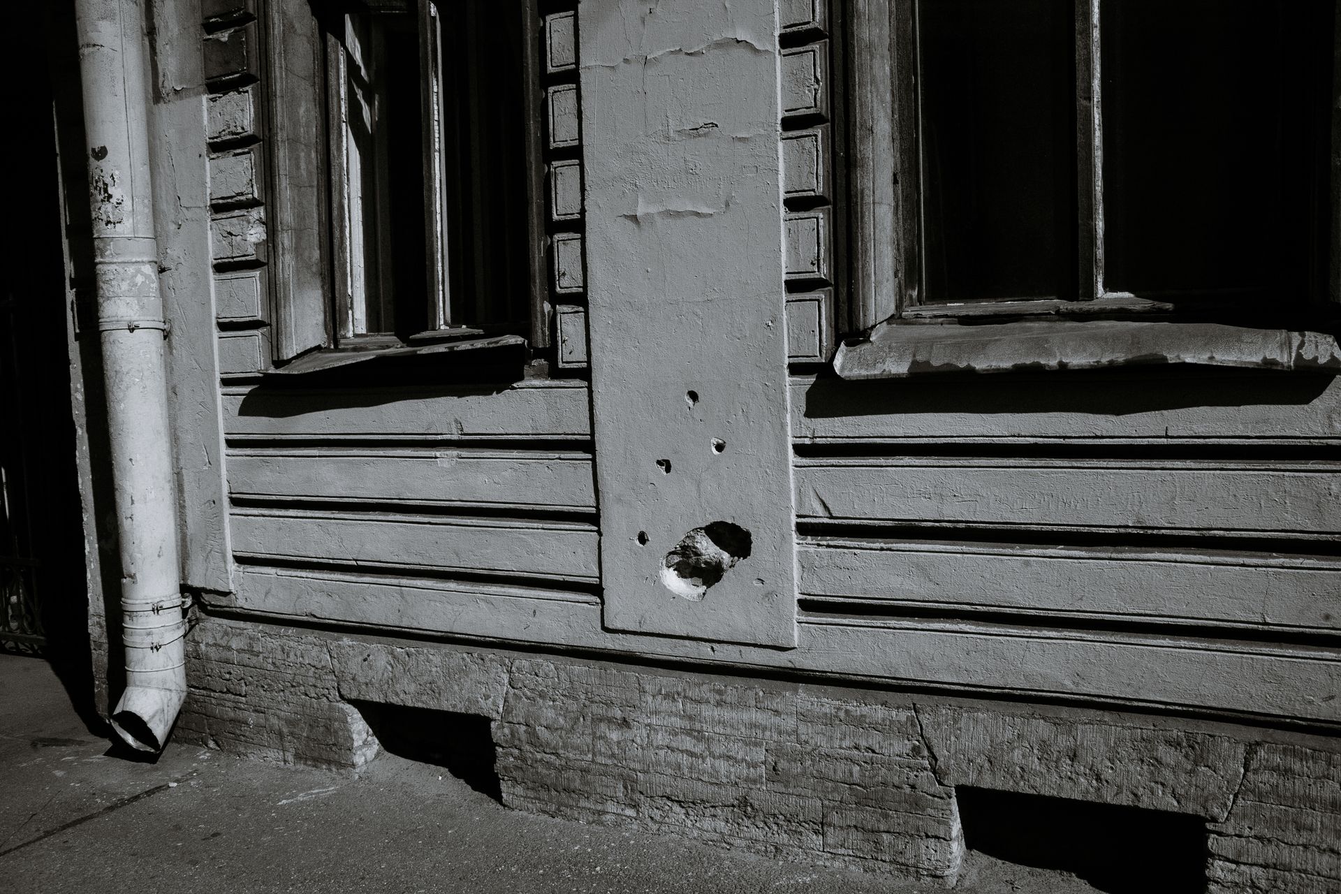 Abandoned urban building with broken windows and visible wall damage in black and white.