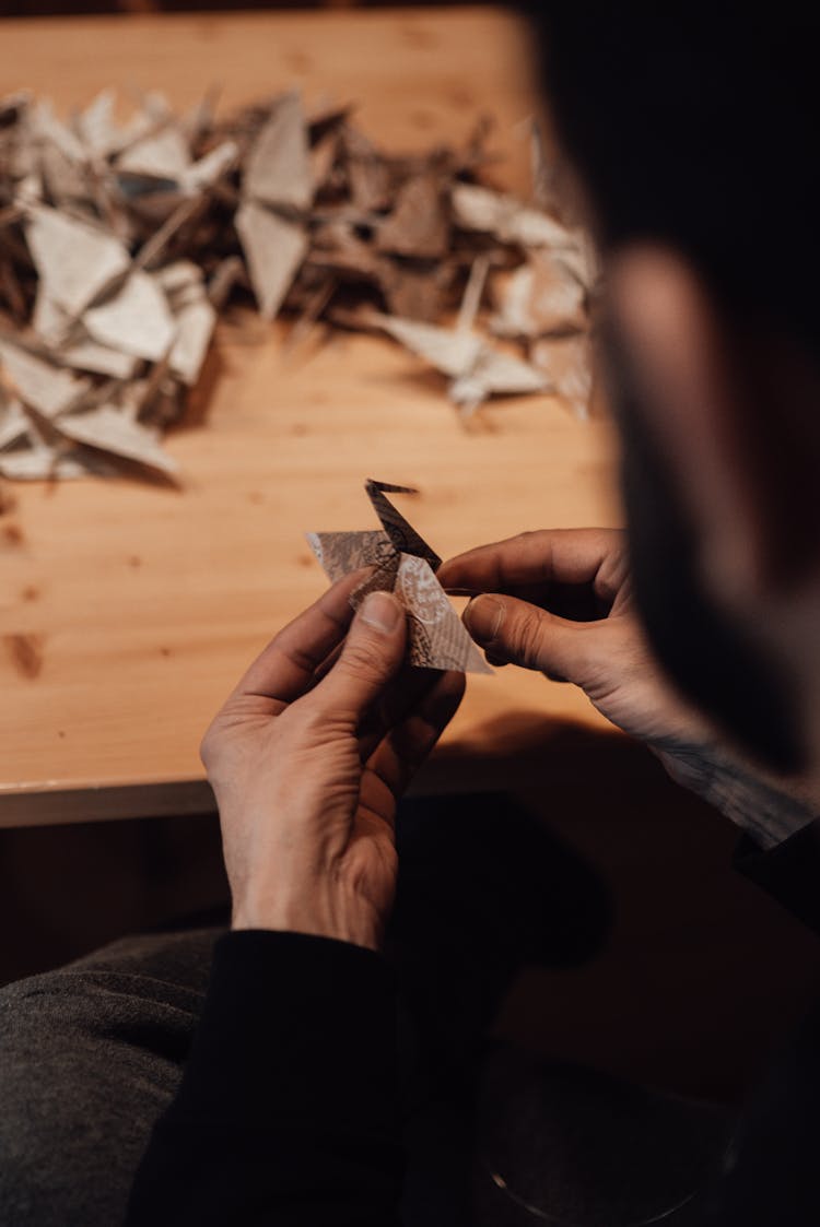 Anonymous Male Creating Origami Crane Near Table In Workshop