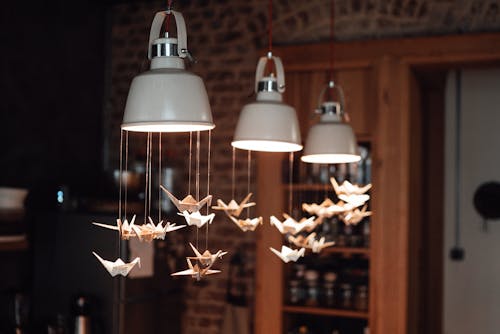 Interior of light restaurant with white lamps decorated with origami paper cranes near brick wall and shelves with utensil