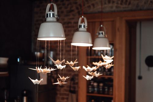 Free Interior of light restaurant with white lamps decorated with origami paper cranes near brick wall and shelves with utensil Stock Photo