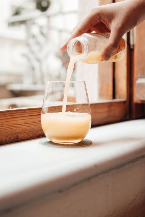 Free Crop faceless lady pouring orange cocktail from small bottle in glass on windowsill near window in bright room Stock Photo