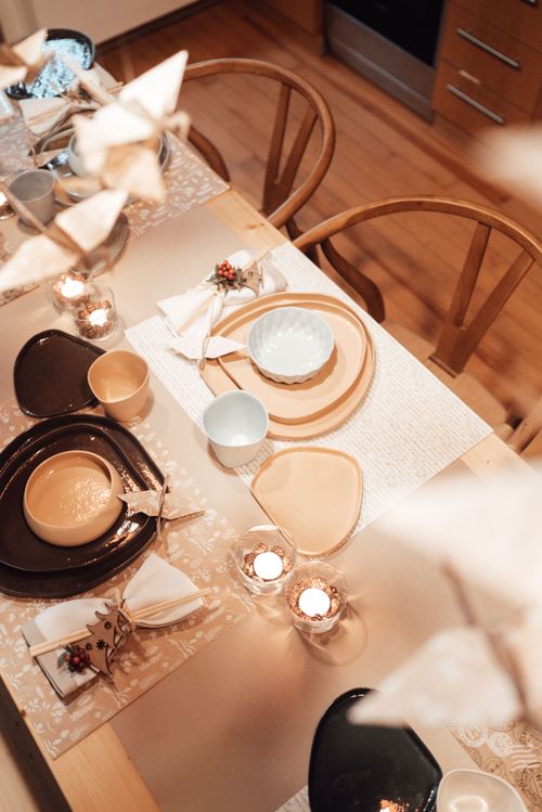 Free Top view of table served with various dishware and burning candles in kitchen with wooden chairs and hanging paper cranes Stock Photo