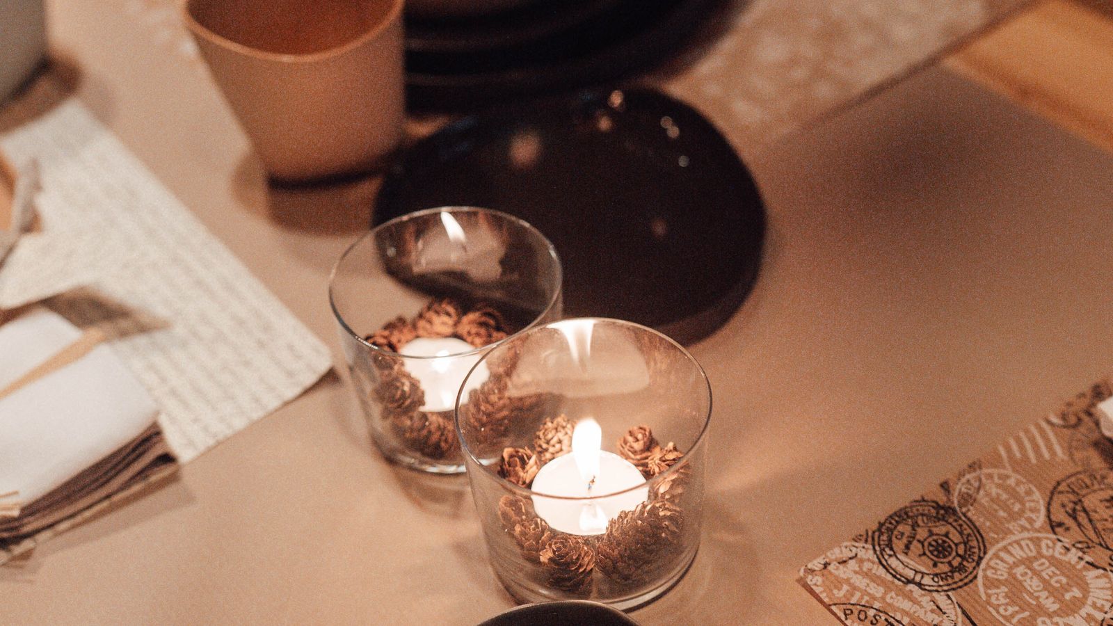 Two lit candles in glass holders beside cups and tableware