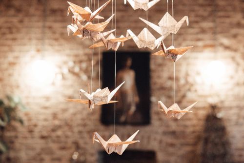 Free Various paper cranes hanging in light room against decorative brick wall with glowing lamps and picture at home on blurred background Stock Photo