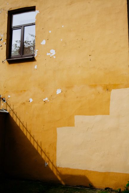 A yellow wall with a window casting a shadow, featuring a rustic texture.