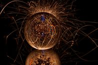 Abstract bright drop with refraction of golden gleams on sparkle background on dark surface with reflection and rays of light