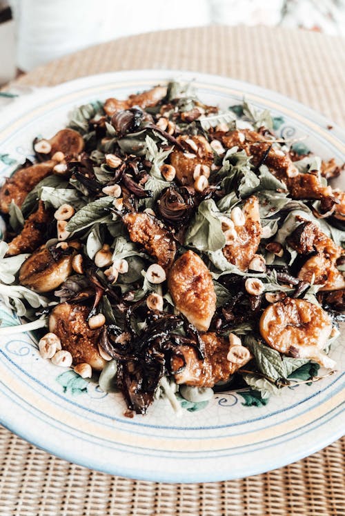 From above tasty healthy fig salad with fresh mixed leaves and nuts served on soup plate in light room