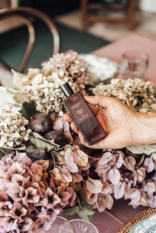 Person showing fragrant perfume against blooming flowers