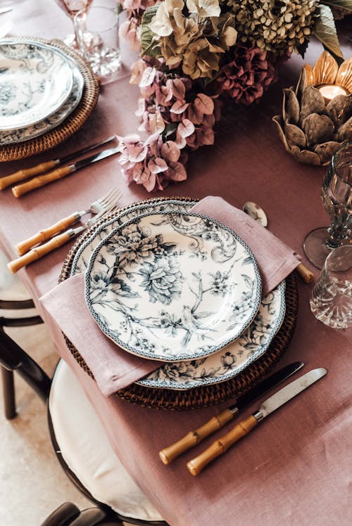 High angle of ceramic plates with napkin placed near cutlery on table decorated with blooming flowers for festive event